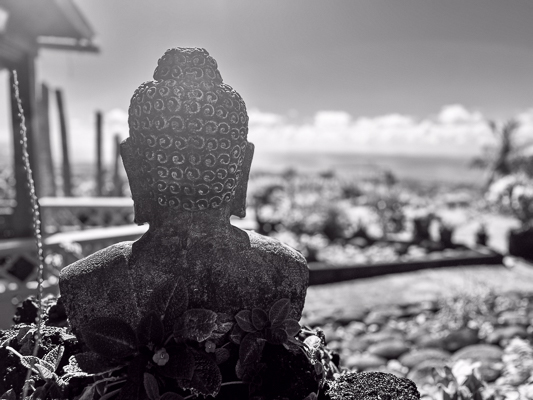 Steinerne Buddha-Figur mit Blick auf tropischen Garten und Meer in der Ferne