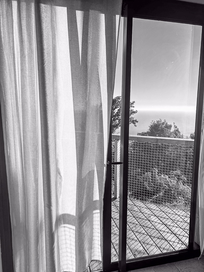 ffener Vorhang mit Blick auf eine sonnige Holzterrasse – Licht fällt weich auf Boden und Stoff.