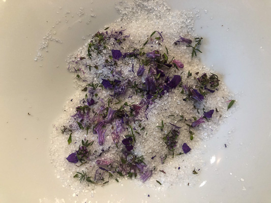 Grobes Salz vermischt mit frischen violetten Blüten und grünen Kräuterteilen