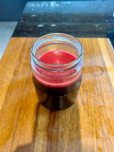 Frisch abgefülltes Johannisbeergelee in einem Glas, dunkelrot leuchtend, auf einer Holzoberfläche.