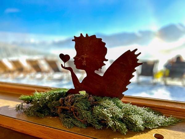 Eine filigrane Elfenfigur mit Herz in der Hand – vor Bergen, Licht und Winterstille. Ein Symbol für stille Einladung und Naturkraft.