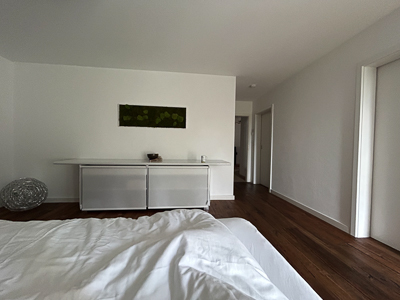Weißer Raum, Blickvom Bett auf Sideboard eine Tasse – der Tag wartet, nicht drängend.