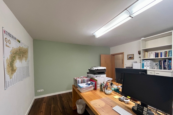Blick ins Arbeitszimmer mit frisch gestrichener Salbeigrün-Wand, Bücherregalen und Schreibtisch.