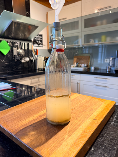 Flasche mit jungem Wein in Gärung, auf Holzbrett in Küche