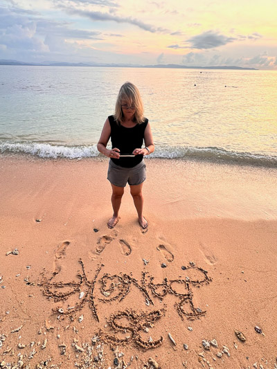 Frau steht am Strand und fotografiert Sandbild