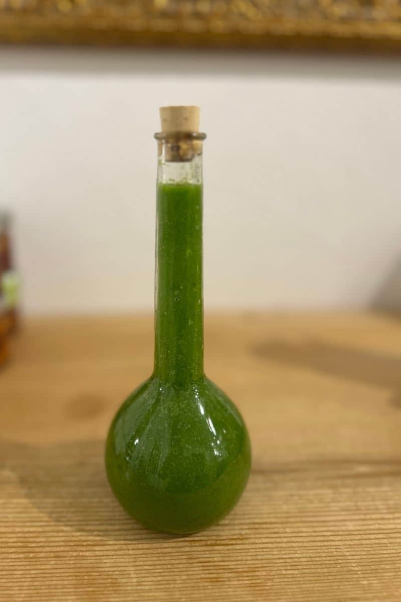 Selbst gemachtes Bärlauchöl in einer bauchigen Glasflasche mit Korken, intensiv grün auf Holzuntergrund.