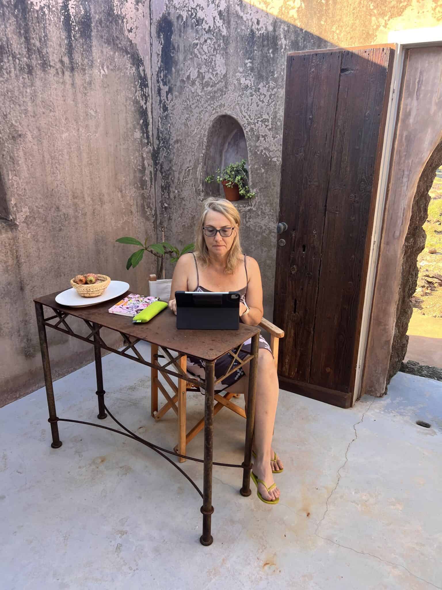 Dagmar Wienböker schreibt auf einem iPad an einem alten Eisentisch auf einer Terrasse in Pantelleria.