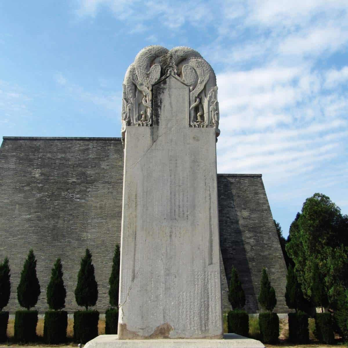 Die wortlose Stele am Qianling-Mausoleum: ein hoher, heller Steinblock mit Drachenrelief an der Krone, auf einem Sockel vor der Grabhügelmauer. Die Fläche trägt schwach erkennbare, später eingeritzte Schriftzeichen.